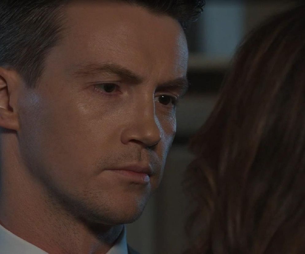 Jakub z M jak miłość w zbliżeniu na twarz, z zamyśloną miną, patrzy na Martynę, której fragment twarzy z ciemnymi włosami widać po prawej stronie. Scena oddaje napięcie emocjonalne przed ślubem Marcina. Więcej o losach bohaterów przeczytasz na Super Seriale.