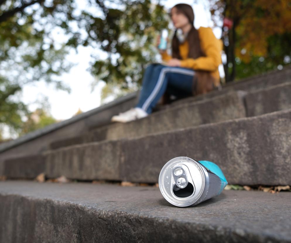 Dziewczyna siedząca na schodach. Na pierwszym planie zgnieciona puszka 