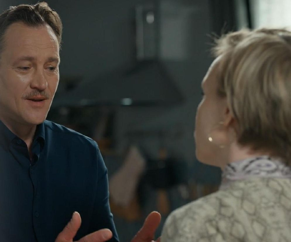 Robert Stefaniak (Paweł Ławrynowicz) z wąsem, w granatowej koszuli, rozmawia z Sonią (Weronika Nockowska), która jest odwrócona tyłem, w jasnej bluzce z wzorem. Scena z odcinka serialu Barwy szczęścia, gdzie Stefaniak przeprasza Sonię za pobicie, ale ona nie odejdzie od oprawcy. Więcej o ich relacji i dramacie Soni przeczytasz na Super Seriale.