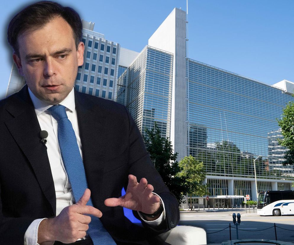 Minister finansów Andrzej Domański w eleganckim garniturze i krawacie, gestykuluje podczas rozmowy, z tłem siedziby Banku Światowego w Waszyngtonie. Kontekst dotyczy negocjacji finansowania polskiej energetyki atomowej, o czym przeczytasz na portalu Super Biznes.
