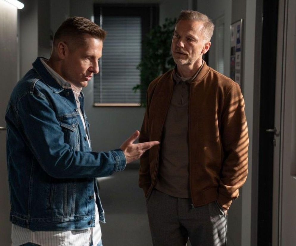 Paweł Zduński (Rafał Mroczek) w dżinsowej kurtce rozmawia z Andrzejem Budzyńskim (Krystian Wieczorek) w brązowej kurtce, którzy stoją na korytarzu. Budzyński podejmie się obrony Pawła w sprawie oskarżenia. Więcej o ich losach dowiesz się na Super Seriale.