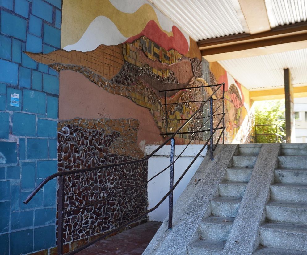 Schody prowadzące do wejścia budynku na osiedlu Słowackiego w Lublinie, wyróżniające się artystyczną mozaiką na ścianie z elementami ceramicznymi i abstrakcyjnymi wzorami, nawiązując do stylistyki PRL. To przykład unikatowej architektury, o której można przeczytać na Architektura Murator Plus.