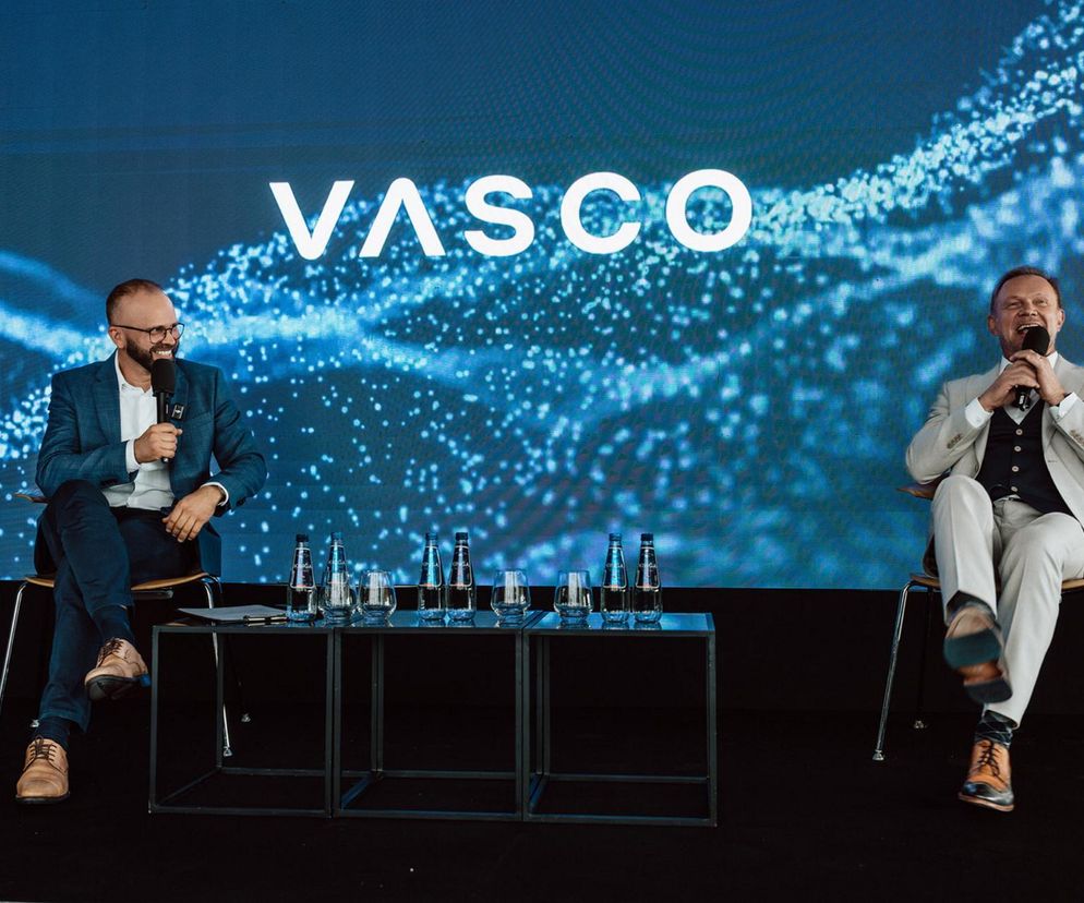 Maciej Góralski i Cezary Pazura na scenie podczas premiery Vasco Translator Q1. Góralski w granatowej marynarce, Pazura w jasnym garniturze z mikrofonem. Prezentacja nowości Vasco Electronics, o której możesz przeczytać na Super Biznes.