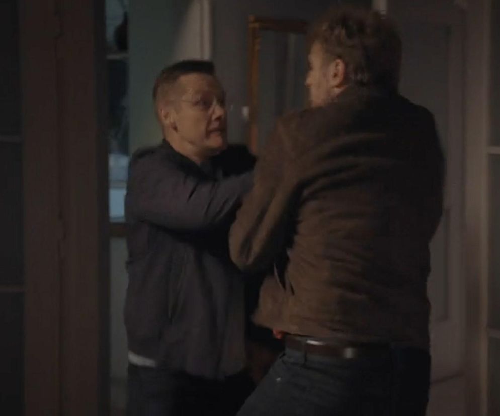 Piotrek (Marcin Mroczek) w szarej koszuli, w okularach, szarpie się z Dariuszem Hoffmanem (Mateusz Rusin) w brązowej kurtce, zasłaniającym twarz. Scena przedstawia walkę, która uratuje Kingę przed molestowaniem w serialu M jak miłość. Więcej o tym na Super Seriale.