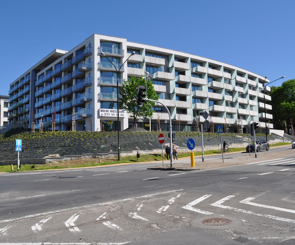 Nowoczesny budynek Apartamentów Reduta w Lublinie z jasną elewacją i przeszklonymi balkonami, usytuowany przy ruchliwej ulicy. Projekt JPA – Jabłoński Pracownia Architektoniczna, prezentowany w konkursie Życie w Architekturze 2025. Więcej o architekturze tego typu na portalu Architektura Murator Plus.