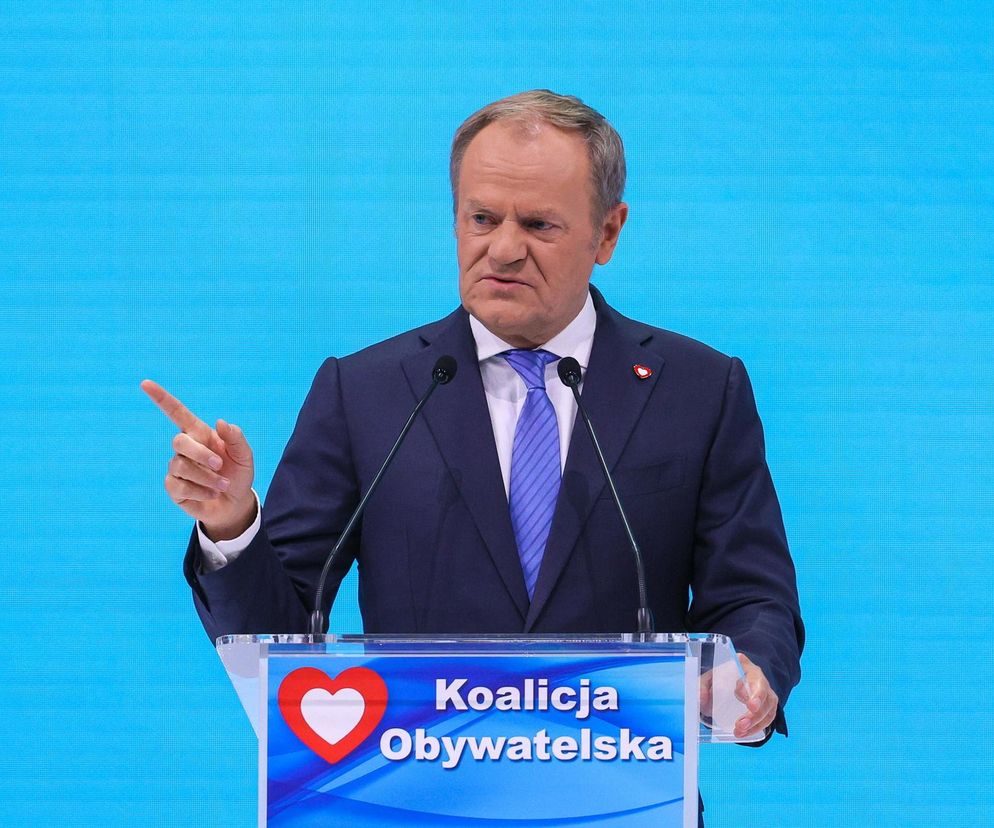 Donald Tusk, Premier RP, podczas konferencji prasowej, przemawiający za mównicą z logo Koalicji Obywatelskiej, podnoszący palec wskazujący. Mówi o nowelizacji Karty Nauczyciela. Więcej o zmianach dla nauczycieli przeczytasz na portalu Super Biznes.