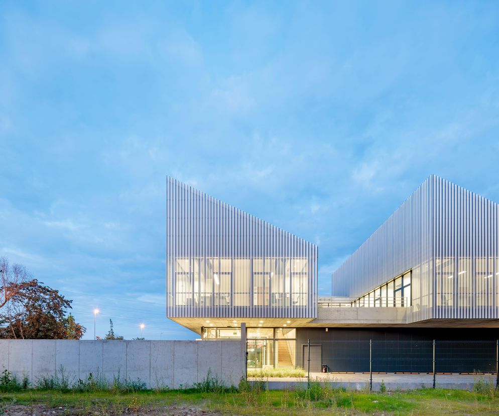 Nowoczesna siedziba firmy PRIME Construction w Szczecinie, zaprojektowana przez Orłowski, Szymański - Architekci, z charakterystycznymi jednospadowymi dachami i fasadą z perforowanej blachy, widoczna w wieczornym świetle. Więcej o innowacyjnych projektach na Architektura Murator Plus.