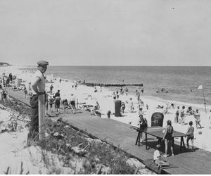 Plażowicze podczas wypoczynku. Widoczny drewniany deptak, wiklinowe kosze plażowe oraz stół do ping-ponga. Zdjęcie zrobiono w okresie pomiędzy 1918-1937 roku w Juracie 