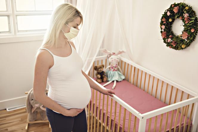 kobieta w ciąży spoglądająca na dziecięce łóżeczko