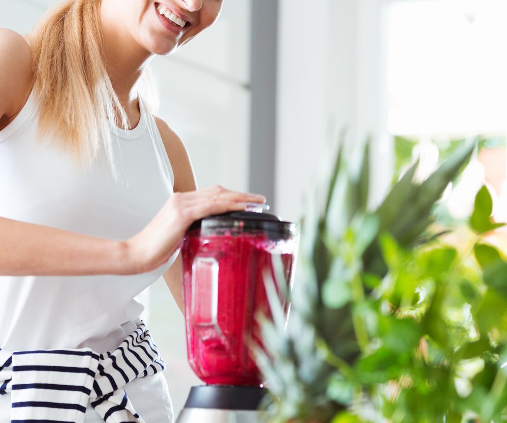 Uśmiechnięta kobieta robi smoothie w blenderze