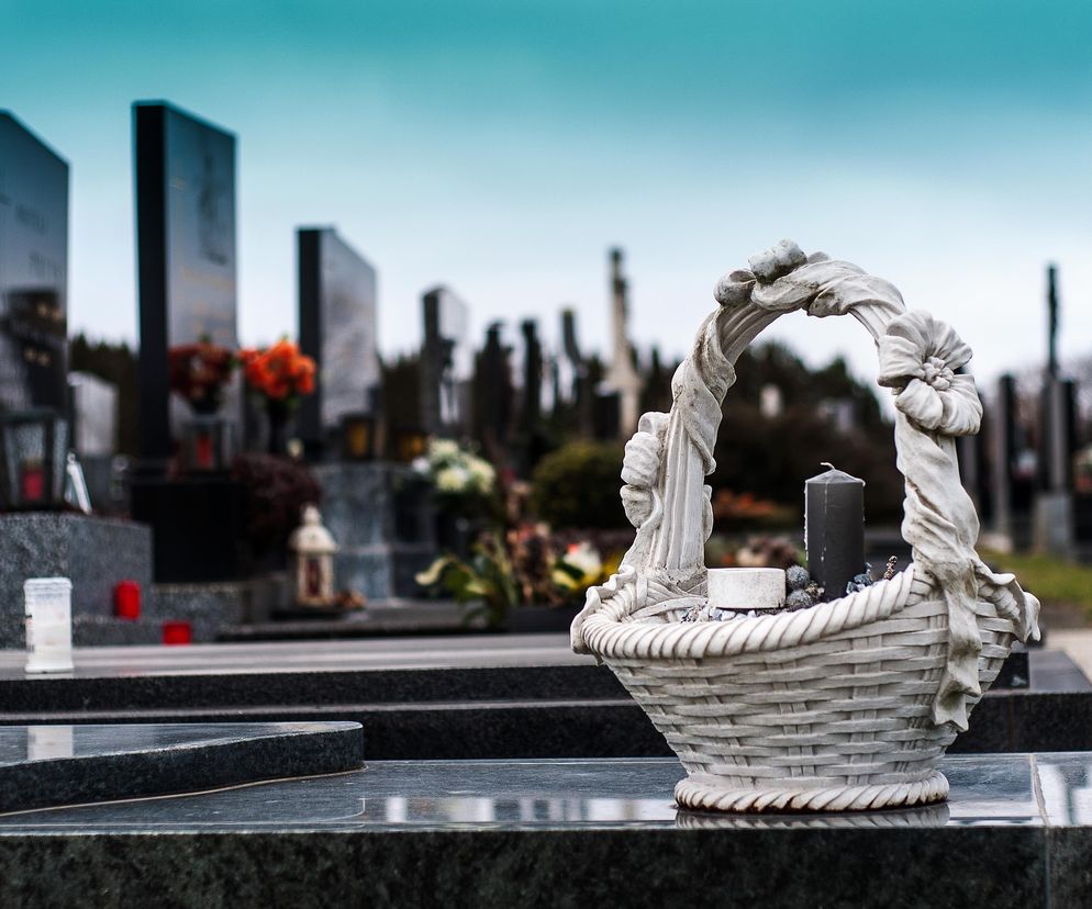 Kamienna dekoracja w kształcie koszyczka z czarną świecą na nagrobku, symbolizująca pamięć o zmarłych i problem kradzieży na cmentarzach. O tych wstrząsających przypadkach możesz przeczytać na Super Biznes.