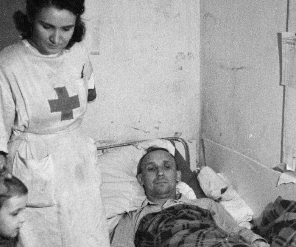 Fotografia z Powstania Warszawskiego. Śródmieście Północne. Szpital kompanii Koszta w budynku dawnego Towarzystwa Ubezpieczeń Rosja przy ul. Marszałkowskiej 124/128, róg Moniuszki 11. Przy rannym powstańcu sanitariuszka Janina Stęczniewska Inka z Wojskowej Służby Kobiet z córką Hanią