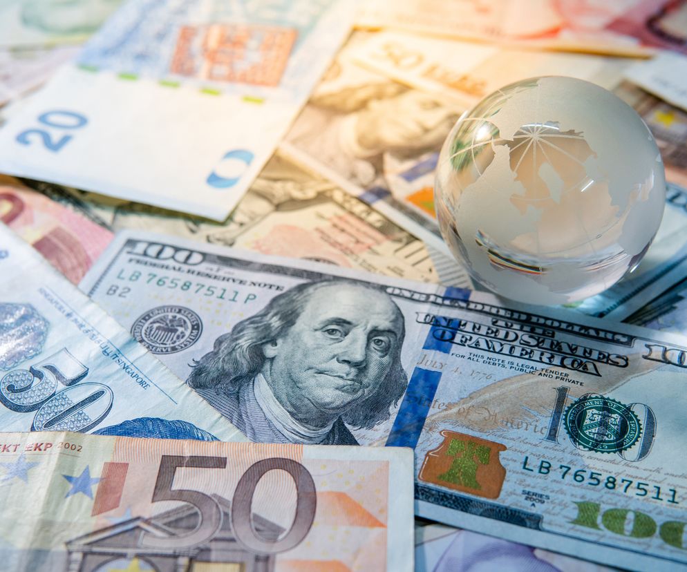 Różnorodne banknoty walut międzynarodowych, takie jak dolary, euro i funty, rozsypane na stole, z umieszczonym na nich szklanym globusem. Obraz symbolizuje globalny rynek finansowy i zmienność kursów walut, w tym osłabienie złotego, co szczegółowo analizuje Super Biznes w artykule o notowaniach walut na 8 września 2025 roku.