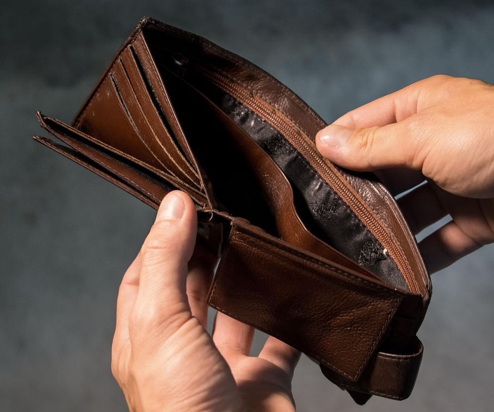 Otwarty, pusty, brązowy portfel trzymany w dłoniach, symbolizujący brak pieniędzy i problemy finansowe. Scena podkreśla trudności z egzekucją komorniczą i kwotami wolnymi od potrąceń, o których przeczytasz więcej na portalu Super Biznes.