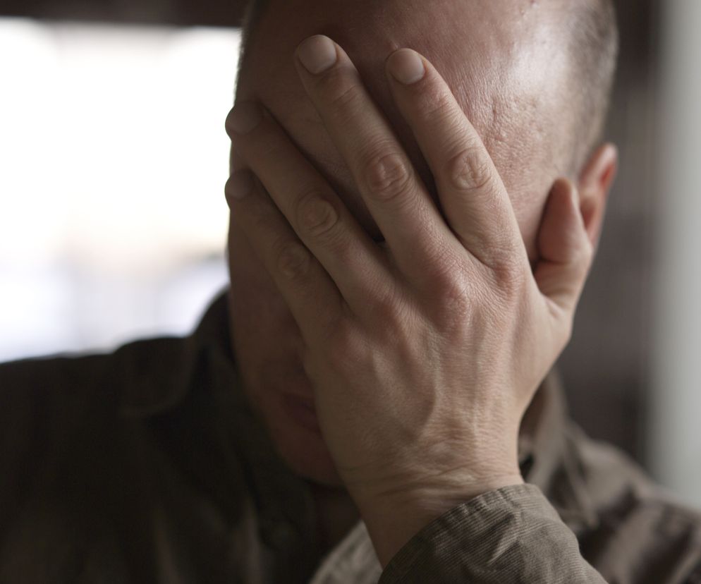 Przygnębiony mężczyzna trzyma rekę na twarzy.