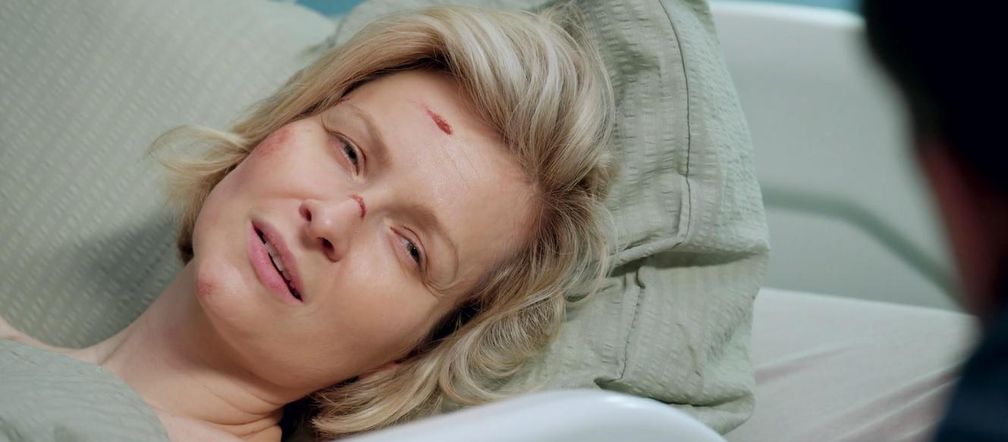 Marieta Żukowska jako Bożena w szpitalu, z widocznymi obrażeniami na twarzy po wypadku samochodowym. Aktorka leży na poduszce, a jej spojrzenie skierowane jest poza kadr, odzwierciedlając dramatyczny moment z serialu Barwy szczęścia. Więcej o losach bohaterki na Super Seriale.