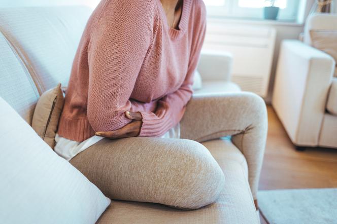 Kobieta z bolącym brzuchem siedzi na kanapie