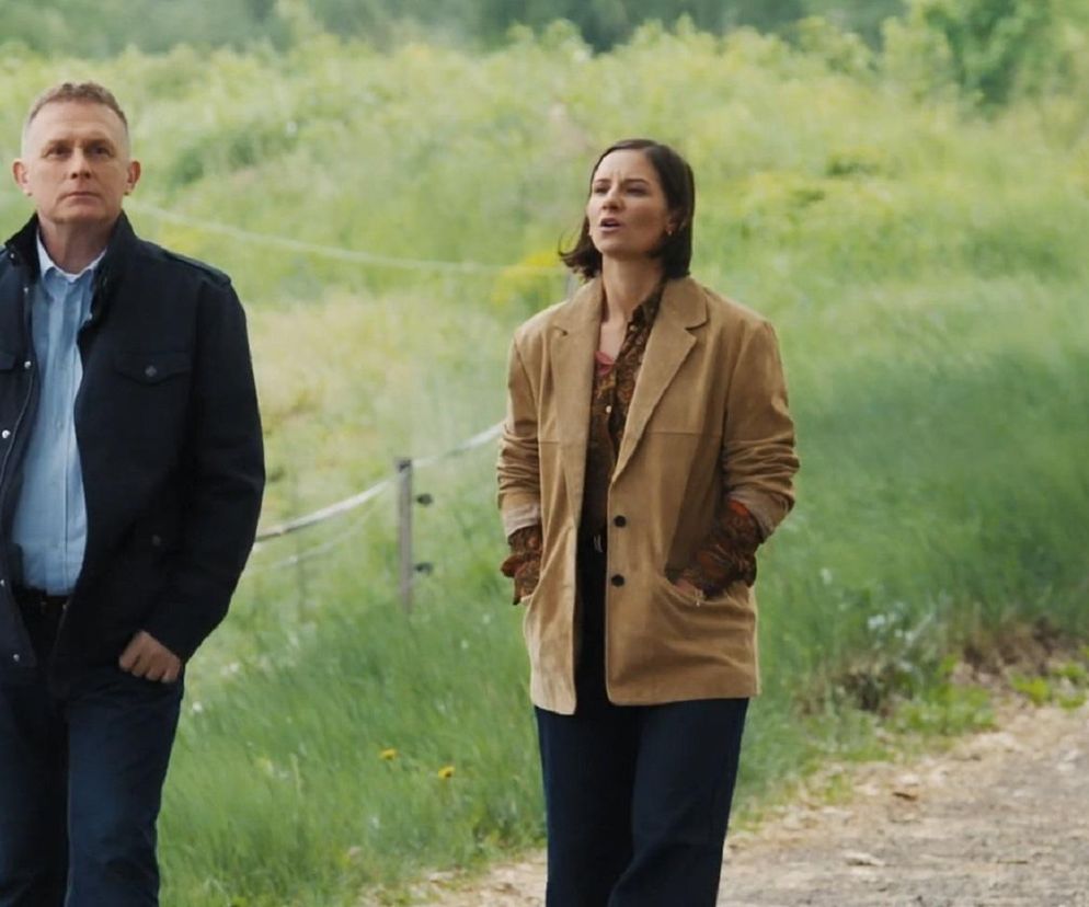 Artur Rogowski (Robert Moskwa) i Agnes (Amanda Mincewicz) w serialu M jak miłość stoją na wiejskiej drodze w otoczeniu zieleni. Artur w niebieskiej kurtce i koszuli, Agnes w beżowej marynarce i wzorzystej bluzce. Możesz przeczytać więcej o serialach na portalu Super Seriale.