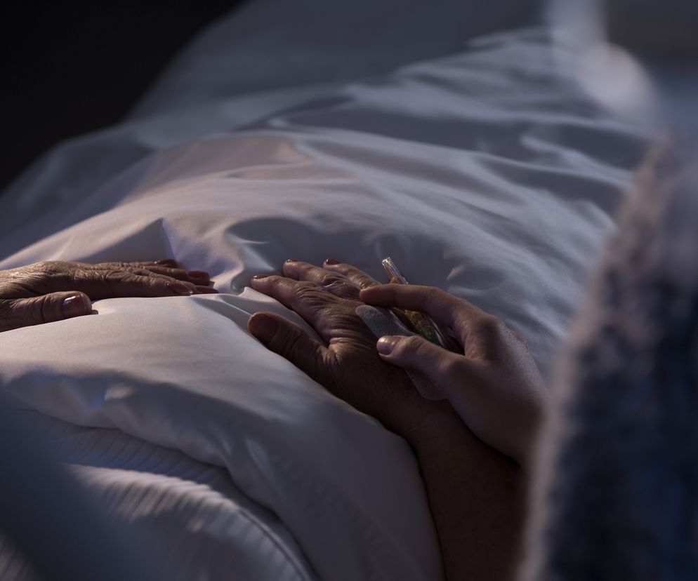 zbliżenie na dłonie osoby leżącej na szpitalnym łóżku i jej gościa