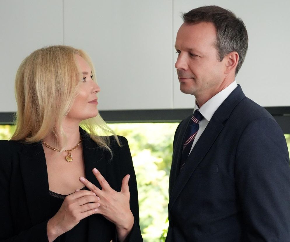 Karolina (Marta Dąbrowska) i Bruno (Lesław Żurek) rozmawiają, stojąc naprzeciwko siebie; Karolina w czarnej marynarce z biżuterią na szyi gestykuluje, Bruno w garniturze i krawacie patrzy na nią. Zdjęcie ilustruje odcinek serialu Barwy szczęścia, a więcej na ten temat przeczytasz na Super Seriale.