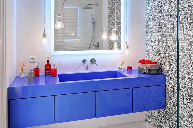 Łazienka z niebieskimi szafkami, tapetą i cegłą