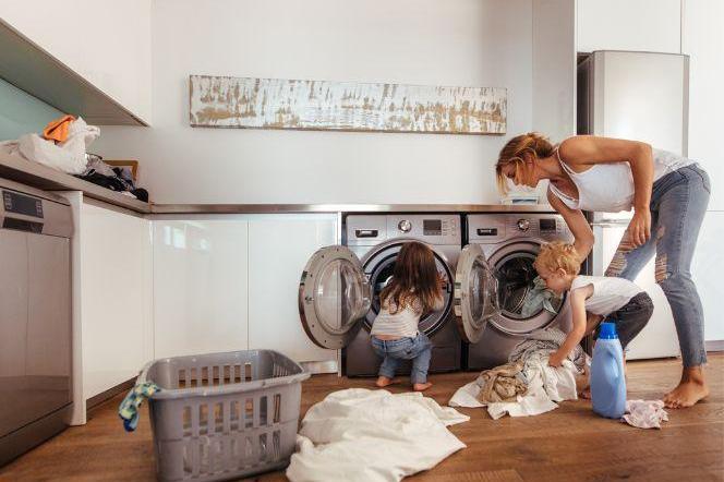 kobieta z dójką dzieci wrzucają ubrania do pralki
