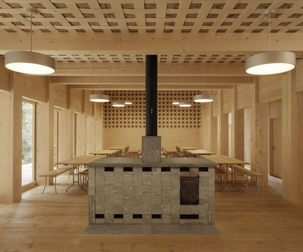 Wielofunkcyjna hala w Vrin projektu Giona Antoniego Caminady z kamiennym piecem centralnym i drewnianymi stołami. Na suficie widoczny pleciony wzór. O zastosowaniu drewna w architekturze, czytaj więcej na Architektura Murator Plus.