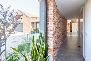 Ceglana ściana korytarza nawiązuje do elewacji domu widocznej przez szerokie okna