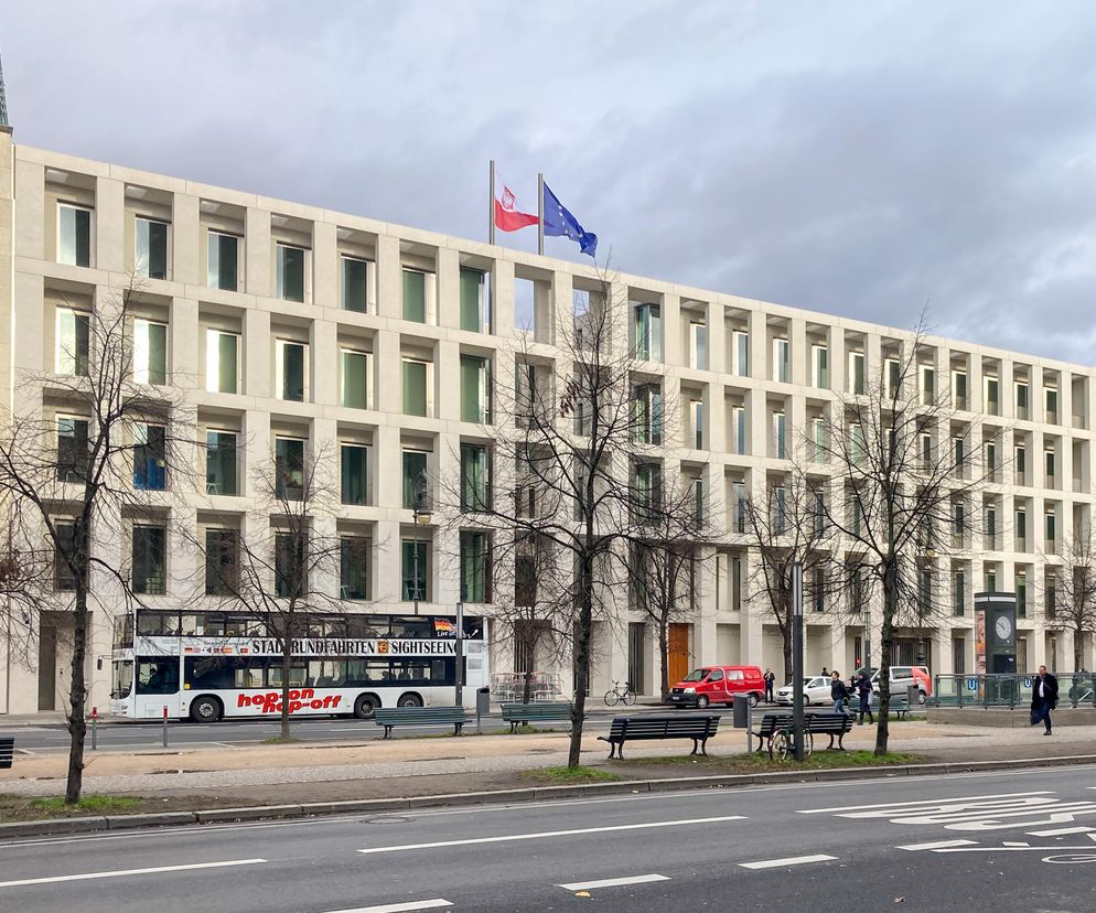 Nowoczesny budynek Ambasady Rzeczypospolitej Polskiej w Berlinie, dzieło JEMS Architekci, z fasadą w neutralnej kolorystyce i o regularnym rytmie okien. Na dachu powiewają flagi Polski i Unii Europejskiej. Informacje o tym obiekcie znajdziesz na Architektura Murator Plus.