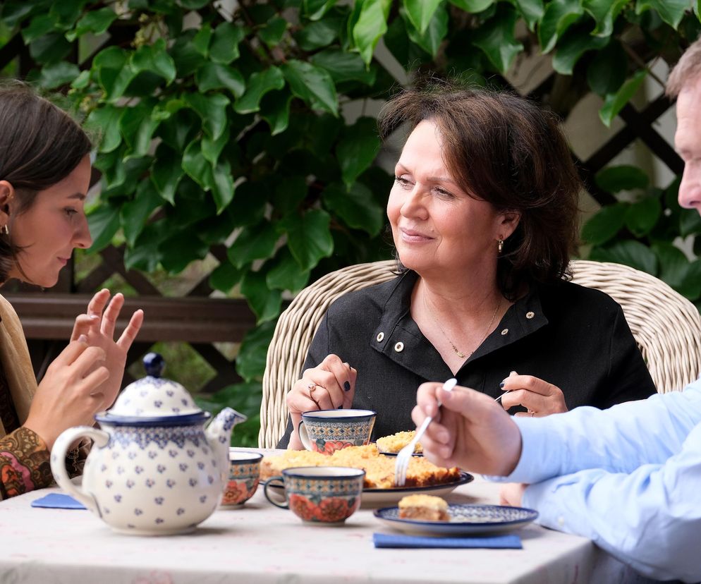 Aktorka Amanda Mincewicz (Agnes) rozmawia z Małgorzatą Pieńkowską (Marysia) i Robertem Moskwą (Artur) przy stole na zewnątrz, podczas posiłku. Agnes, córka Artura, zamieszka w Grabinie, a Marysia przyjmie ją w swoim domu, o czym przeczytasz na Super Seriale.