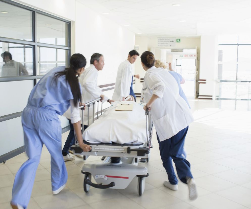 Zespół medyczny w pośpiechu transportujący pacjenta na szpitalnym łóżku, pędzący korytarzem w celu udzielenia pilnej pomocy. Temat gangreny gazowej na wojnie w Ukrainie znajdziesz na Poradnik Zdrowie.