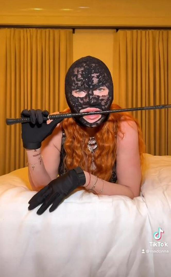 Madonna w kominiarce rzuca się w konwulsjach po łóżku. W ręce trzyma pejcz. "Ocknij się kobieto"