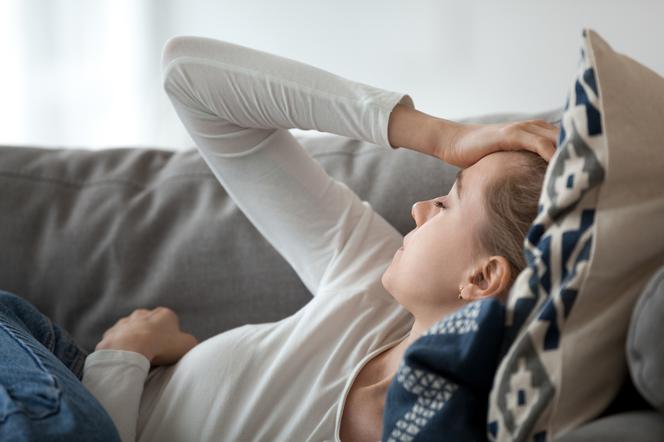 Młoda kobieta leżąca na kanapie, dokucza jej silny ból głowy z przodu. 