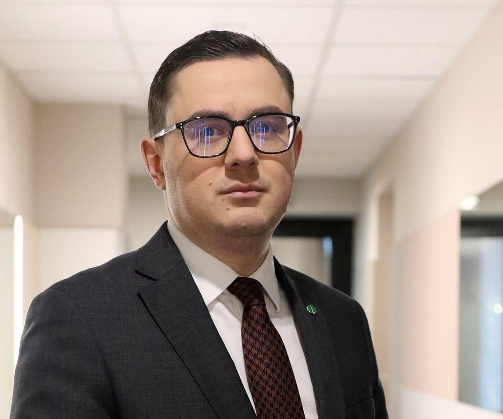 Portret Miłosza Motyki, Ministra Energii, w okularach i garniturze, z zieloną przypinką w klapie, zapowiadającego koniec mrożenia cen prądu od 2026 roku. O skutkach tej decyzji przeczytasz na Super Biznes.