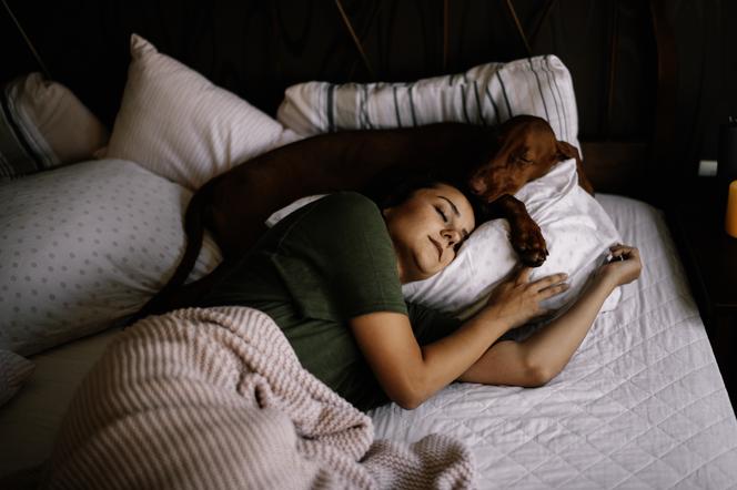 Kobieta śpi w łóżku z psem