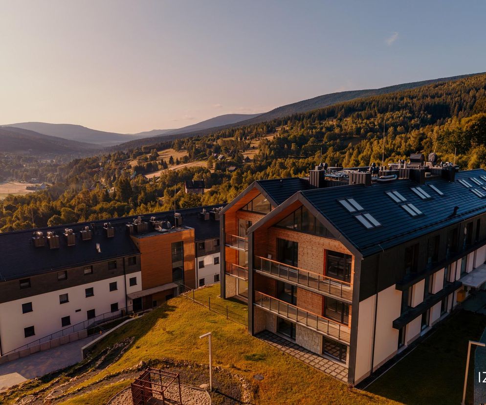 Nowoczesne budynki Izerski Resort w Świeradowie-Zdroju, z elewacjami z łupku, drewna i kamienia, harmonijnie wpisane w górski krajobraz, widok z lotu ptaka o zachodzie słońca. Więcej o konkursie Życie w Architekturze i takich realizacjach na Architektura Murator Plus.