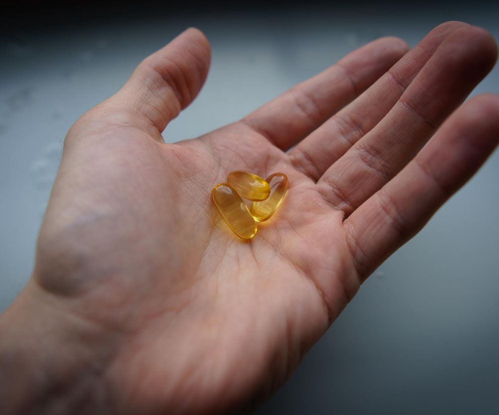 Otwarta dłoń z trzema bursztynowymi kapsułkami omega-3, symbolizująca rozważania nad suplementacją. Kapsułki są miękkie, owalne, odbijają światło. Stanowią odniesienie do artykułu o tym, że omega-3 nie zawsze chroni serce i kiedy może zaszkodzić. Na Poradnik Zdrowie znajdziesz więcej informacji.