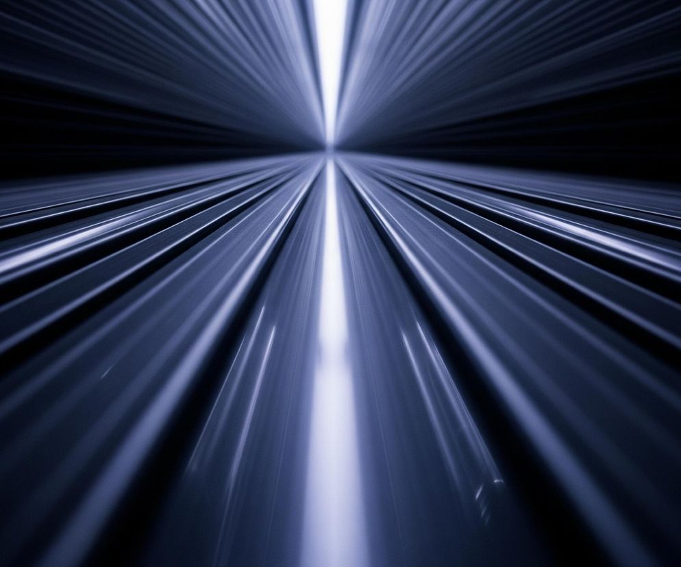 Centralnym punktem obrazu jest tunel lub korytarz, tworzony przez równoległe, lśniące pasy o metalicznym, fioletowo-niebieskim odcieniu. Pasy te rozciągają się od dolnej części kadru ku środkowi, gdzie zbiegają się w jasnym, białym punkcie świetlnym, sugerującym głębię i nieskończoność. Otoczenie po obu stronach korytarza jest ciemne, niemal czarne, co podkreśla intensywność i kierunkowość światła biegnącego przez środek kompozycji.