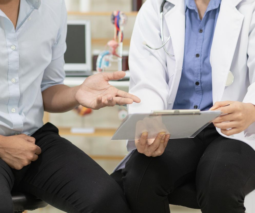 Fragmenty postaci lekarza w białym kitlu ze stetoskopem i pacjenta w jasnoniebieskiej koszuli rozmawiających o zdrowiu mężczyzny, obok widoczny jest model anatomiczny. Temat raka prostaty i profilaktyki można pogłębić na portalu Poradnik Zdrowie.