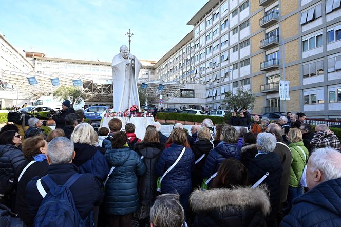 Wierni modlą się o zdrowie Franciszka przed pomnikiem Jana Pawła II. Składają kartki z życzeniami i wiązanki z białych róż