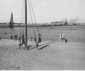 Dzieci na huśtawce na plaży nad morzem Bałtyckim. W tle fragment portu. Miejsce zrobienia zdjęcia Gdynia w okresie 1923-1939