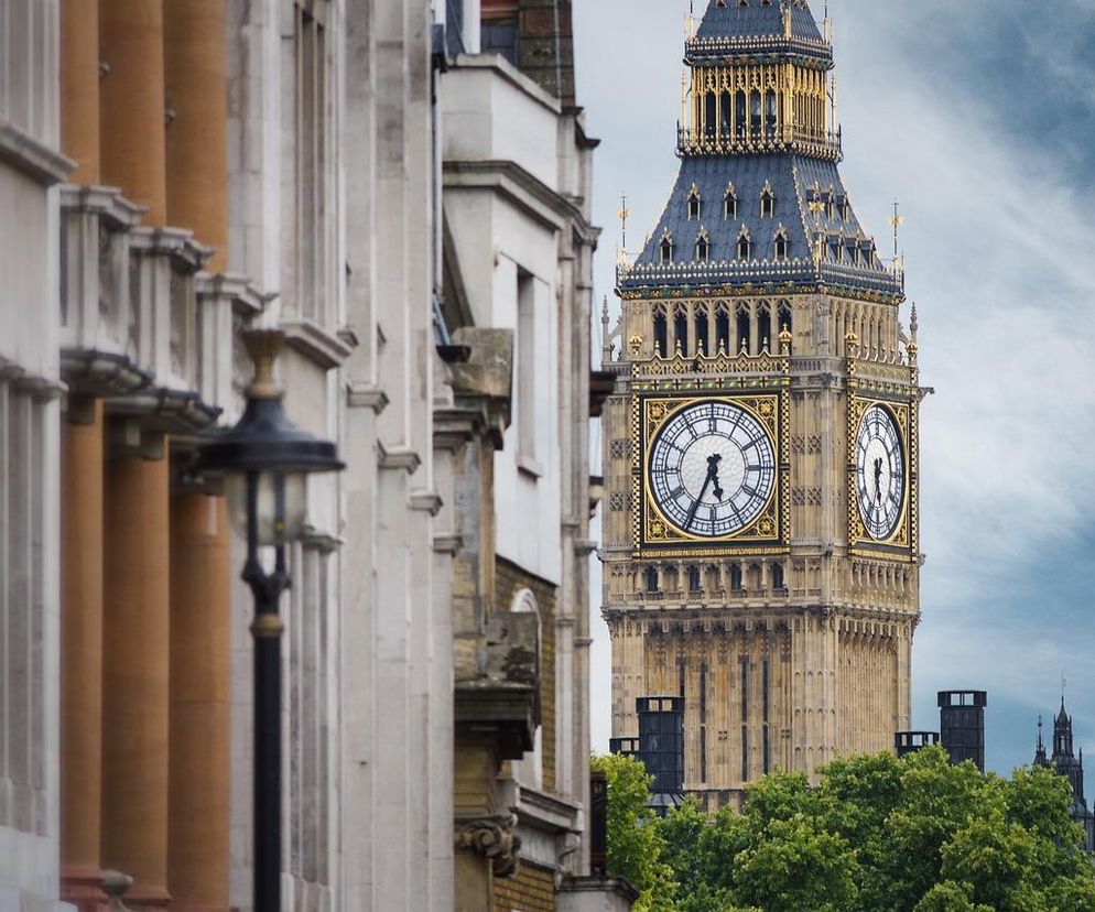 Big Ben w Londynie na tle błękitnego nieba z chmurami, symbolizujący brytyjską gospodarkę i jej wyzwania, o których przeczytasz na Super Biznes. Po lewej stronie widać fragmenty klasycznych budynków z kolumnami.