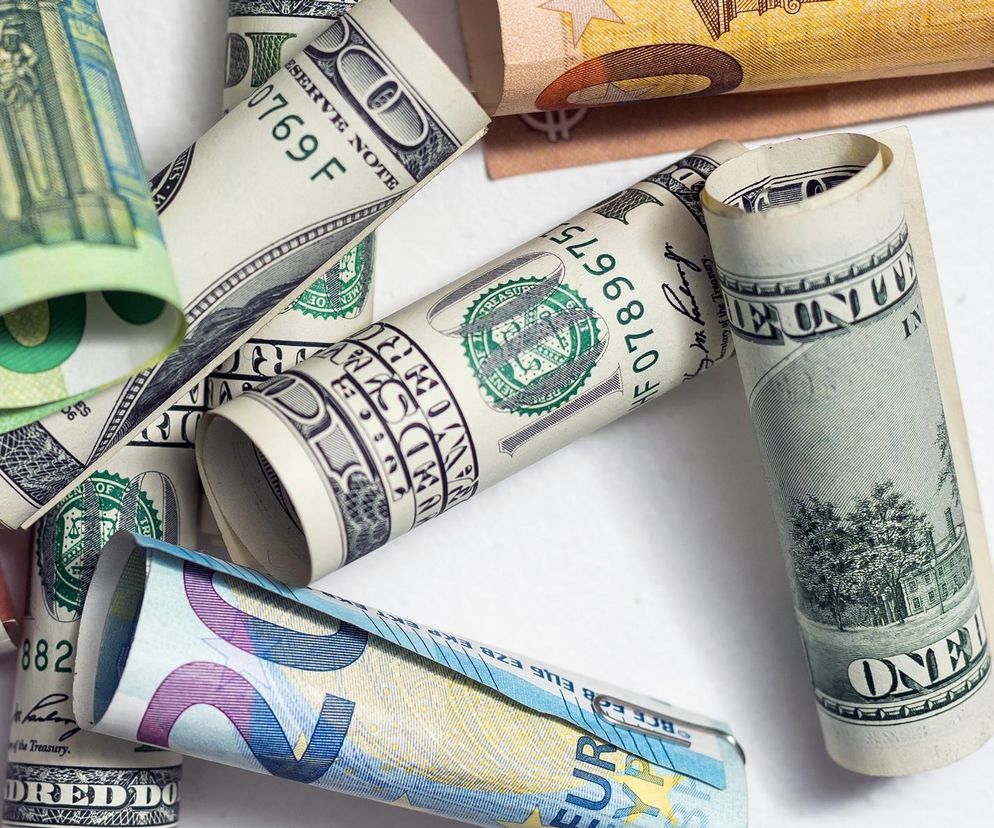 Zwinięte banknoty dolarów amerykańskich i euro na jasnym tle symbolizują dynamikę kursów walut oraz globalne trendy finansowe. O analizie przyczyn siły złotego wobec dolara przeczytasz na Super Biznes.