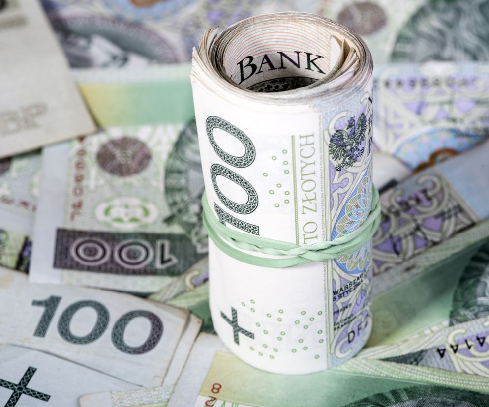 Zrolowane banknoty stuzłotowe, spięte gumką, leżące na rozsypanych pieniądzach, symbolizują bankowość i finanse w kontekście decyzji TSUE w sprawie WIBOR. Szczegóły dotyczące tej kwestii znajdziesz na Super Biznes.