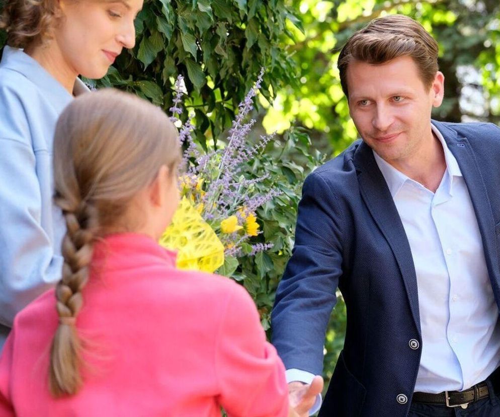 Dominika Suchecka jako Natalka i Wiktoria Basik jako Hania, oglądające Patryka Szwichtenberga w roli Adama Karskiego. Hania trzyma bukiet kwiatów, a Adam patrzy na nią z uśmiechem. Scena związana z serialem M jak miłość, o którym więcej przeczytasz na Super Seriale.