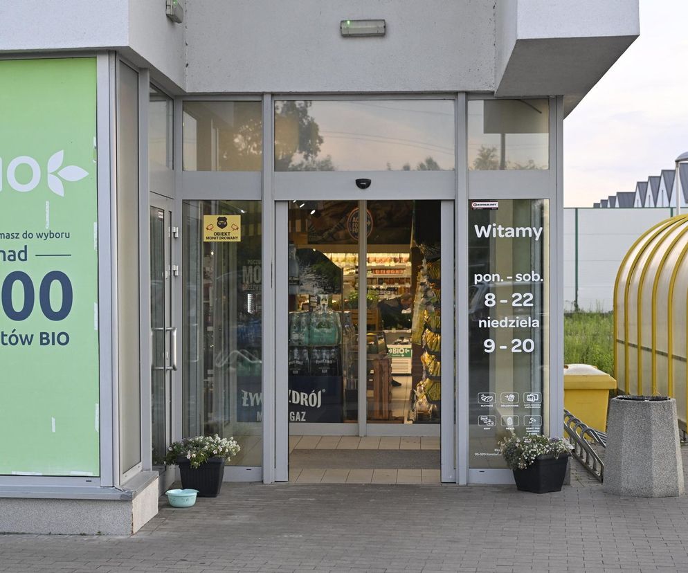 Wejście do sklepu spożywczego „Żywy Zdrój BIO” z widoczną tablicą informującą o godzinach otwarcia, w tym w niedziele od 9:00 do 20:00. To przykład placówki, która może być otwarta w niehandlowe niedziele, o czym możesz przeczytać na Super Biznes.