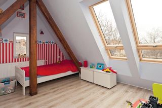 Kącik do spania umieszczono przy ścianie szczytowej. W niej również jest małe okienko, jak w tej po przeciwnej stronie poddasza. Tapeta w pasy wprowadza pogodny nastrój, ale pełni też funkcję ochronną – zabezpiecza ścianę przed zabrudzeniem