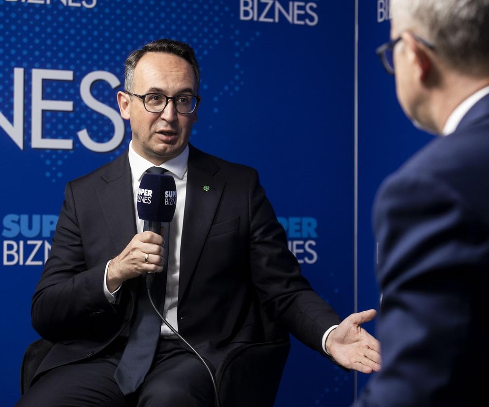 Minister Infrastruktury Dariusz Klimczak w garniturze i okularach, udziela wywiadu, mówiąc do mikrofonu z logo Super Biznes. Rozmowa dotyczy planów i zmian w projekcie Centralnego Portu Komunikacyjnego, o czym szerzej przeczytasz na portalu Super Biznes.