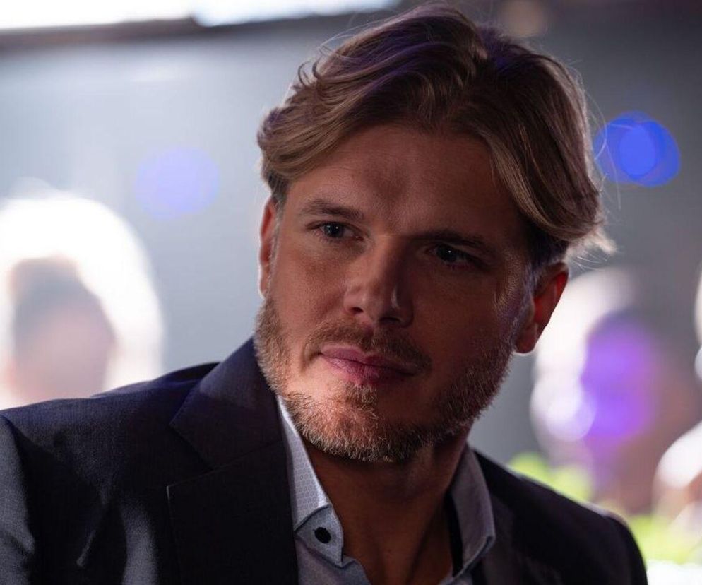 Maks Beger (Tomasz Ciachorowski) w garniturze z rozpiętym kołnierzykiem, patrzy w bok z poważną miną. Na zdjęciu widać jego włosy ułożone do tyłu i starannie przystrzyżoną brodę. Scena dotyczy odcinka serialu Na dobre i na złe, gdzie Beger przypomni sobie, kim jest haker Drago. Więcej o wątku na Super Seriale.