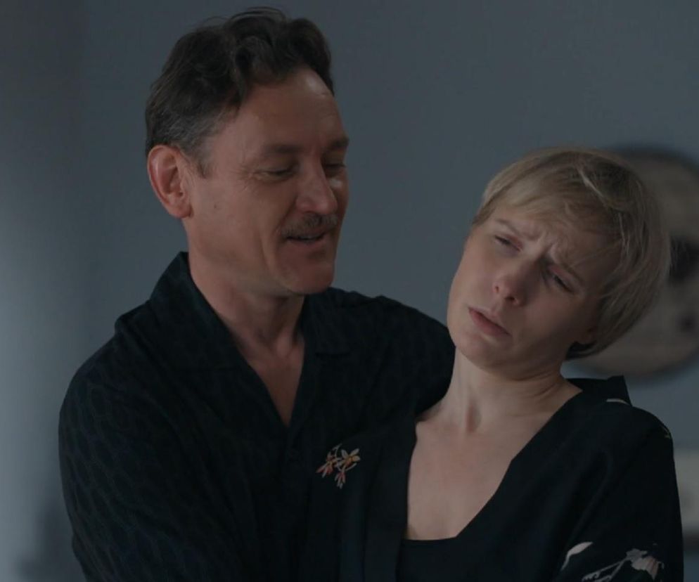 Mężczyzna z wąsem (Robert Stefaniak) obejmujący blondwłosą kobietę (Sonia) w czarnej bluzce, która ma grymas bólu na twarzy. Scena ilustruje jej cierpienie i amnezję po nocy z Bazylowem w serialu Barwy szczęścia. Więcej o tym na Super Seriale.